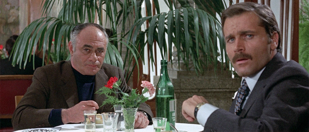 Bonavia points out to Taini the officials gathered at a nearby table