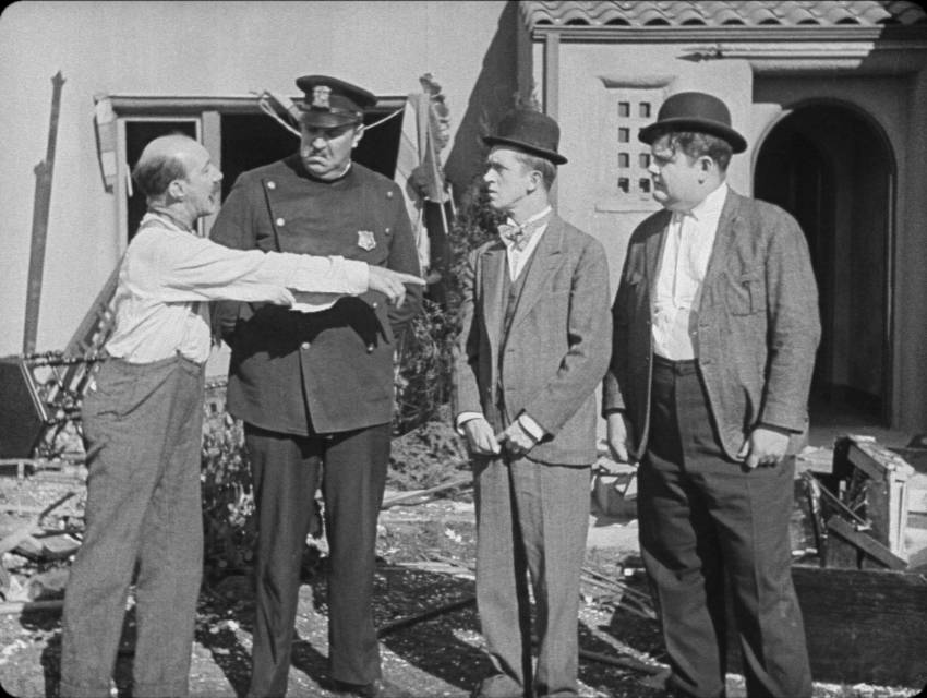 Fin claims to the officer that Stan and Ollie started the fight that has wrecked his home and their car